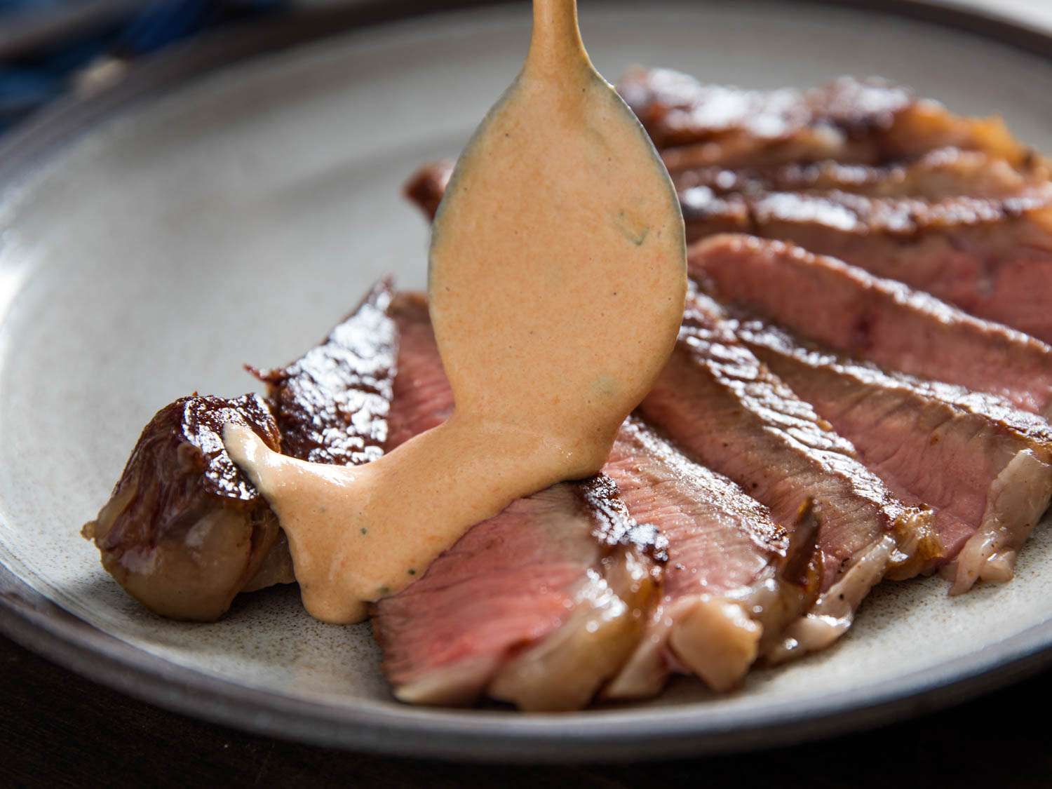 Choron sauce is spooned onto a steak that has been sliced and shingled out on a plate.