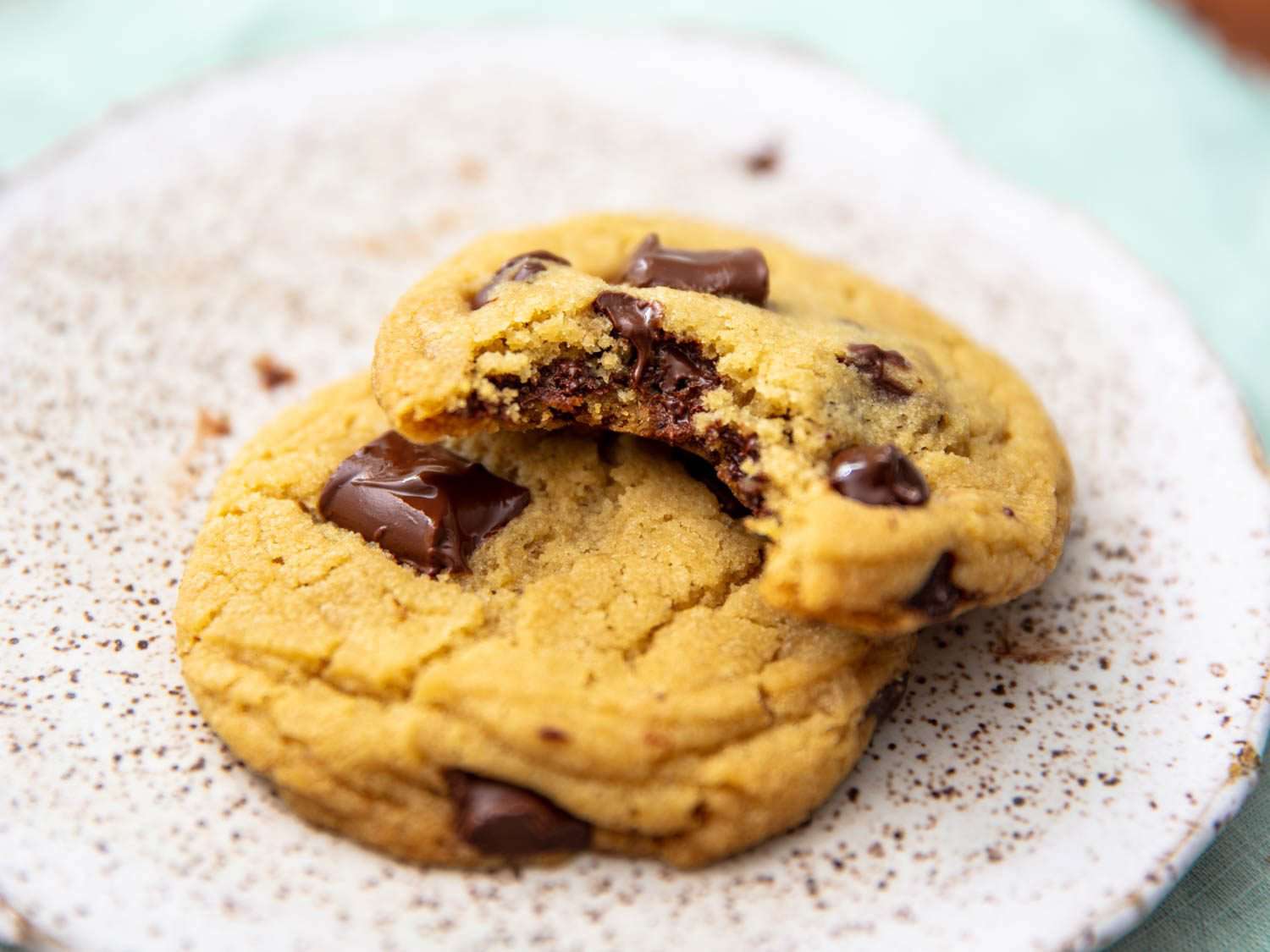Close up of two chocolate chip cookies on a plate, one with a bite missing.