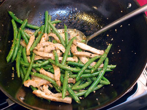 Stir-frying pork strips and green beans together in a wok.