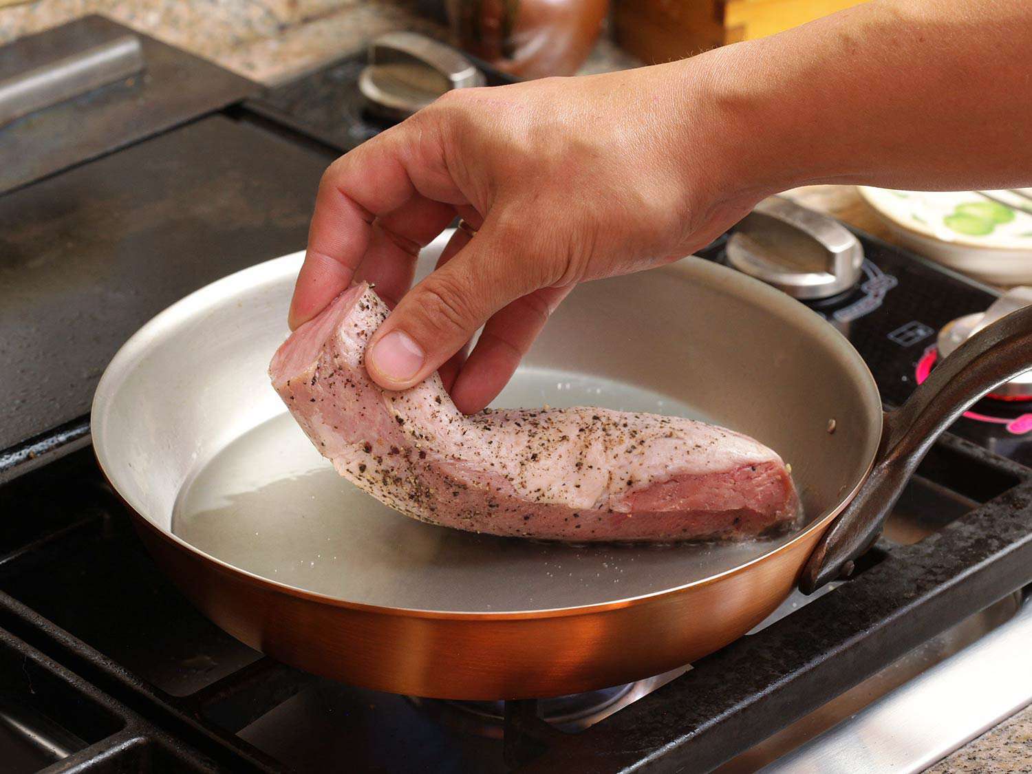 Laying a sous vide pork tenderloin into a hot, oiled skillet to sear before serving.