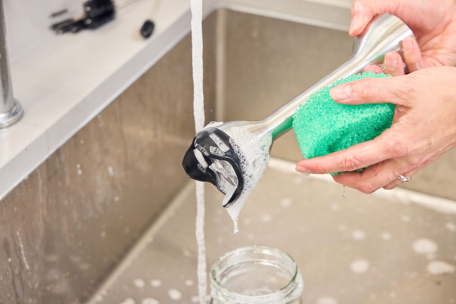 A person washes the Vitamix Immersion Blender in a sink
