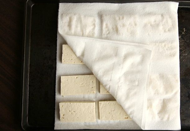 Drying tofu slices between layers of paper towels.