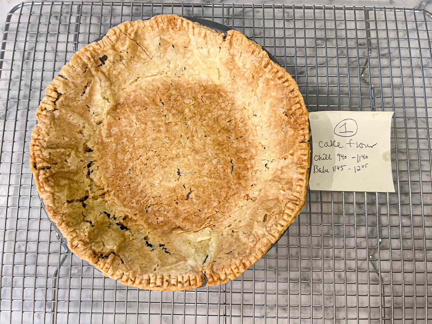 A baked pie crust on a cooling rack with a small note indicating test details nearby