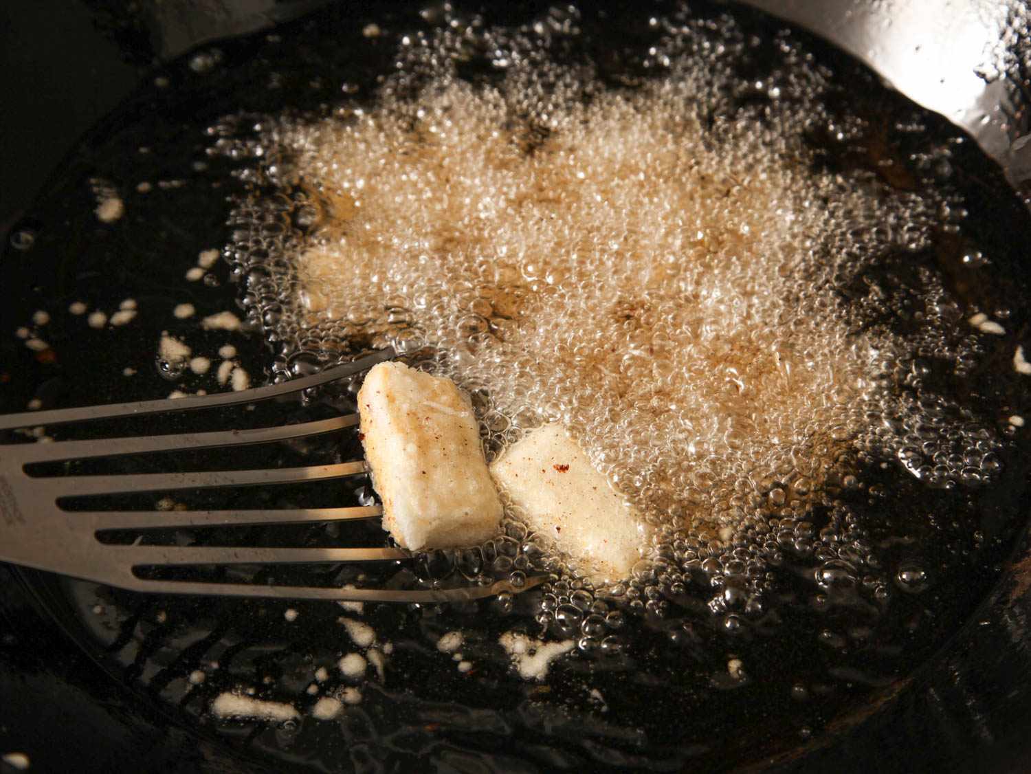 Frying tofu slices until crispy in a wok of hot oil.