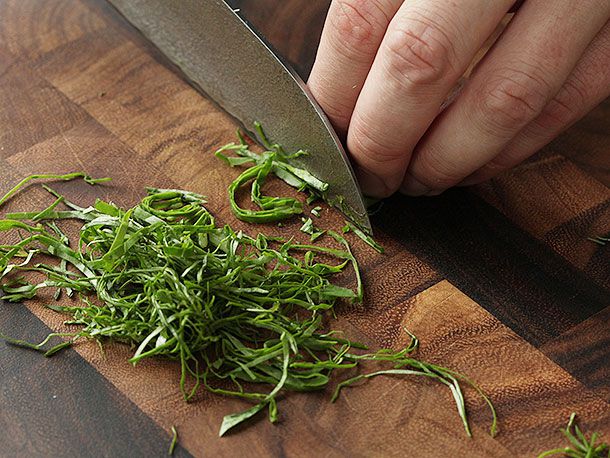 A knife on a cutting board next to a pile of thinly sliced herbs.