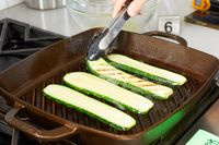 A person flipping zucchinis while they cook on the Smithey Ironware Co. No. 12 Grill Pan.