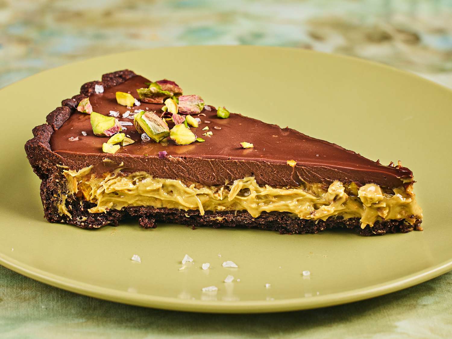 Slice of Dubai Chocolate Tart from a side angle, with layers showing, on a green plate and green tablecloth 