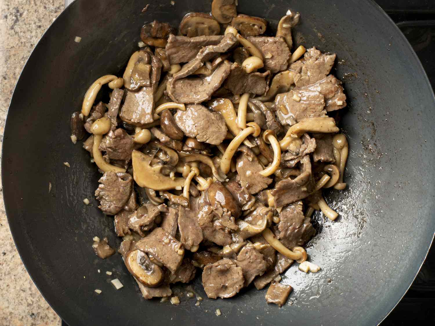 Beef added back to wok, cooked through, and intermingled with the browned mushrooms. The beef and mushrooms are glossy, showing the sauce has been fully emulsified in with the ingredients.