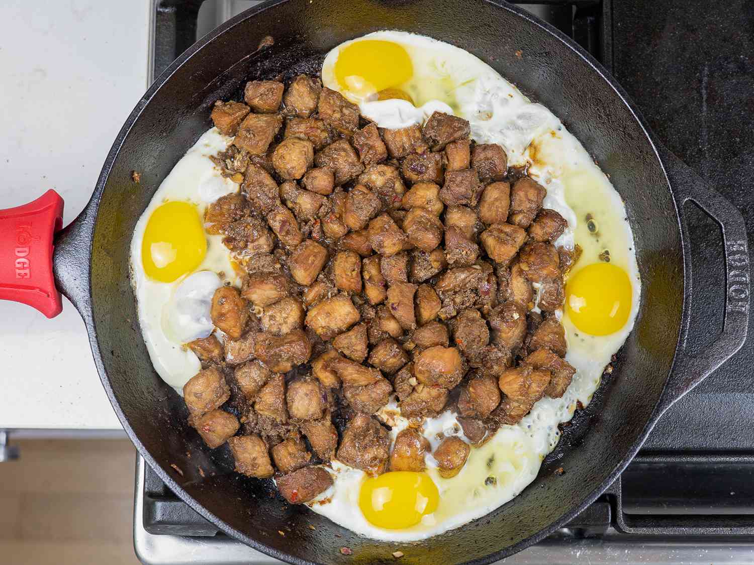 Eggs added to the seasoned, fried pork, all of it in a cast iron pan.