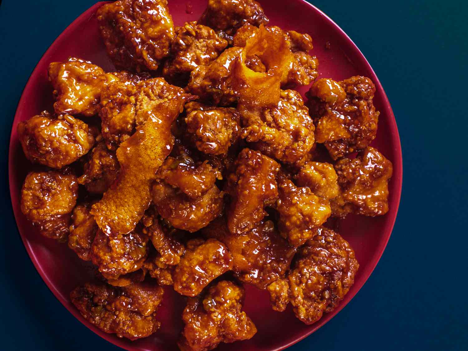 Chinese-American orange chicken on a terracotta-colored platter on a blue background.
