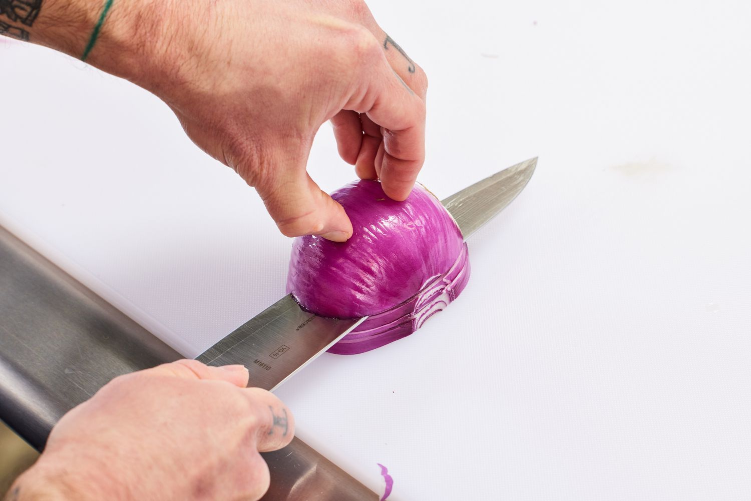Hands slicing a red onion horizontally with a Mercer MX3 8.25-Inch Chef Knife