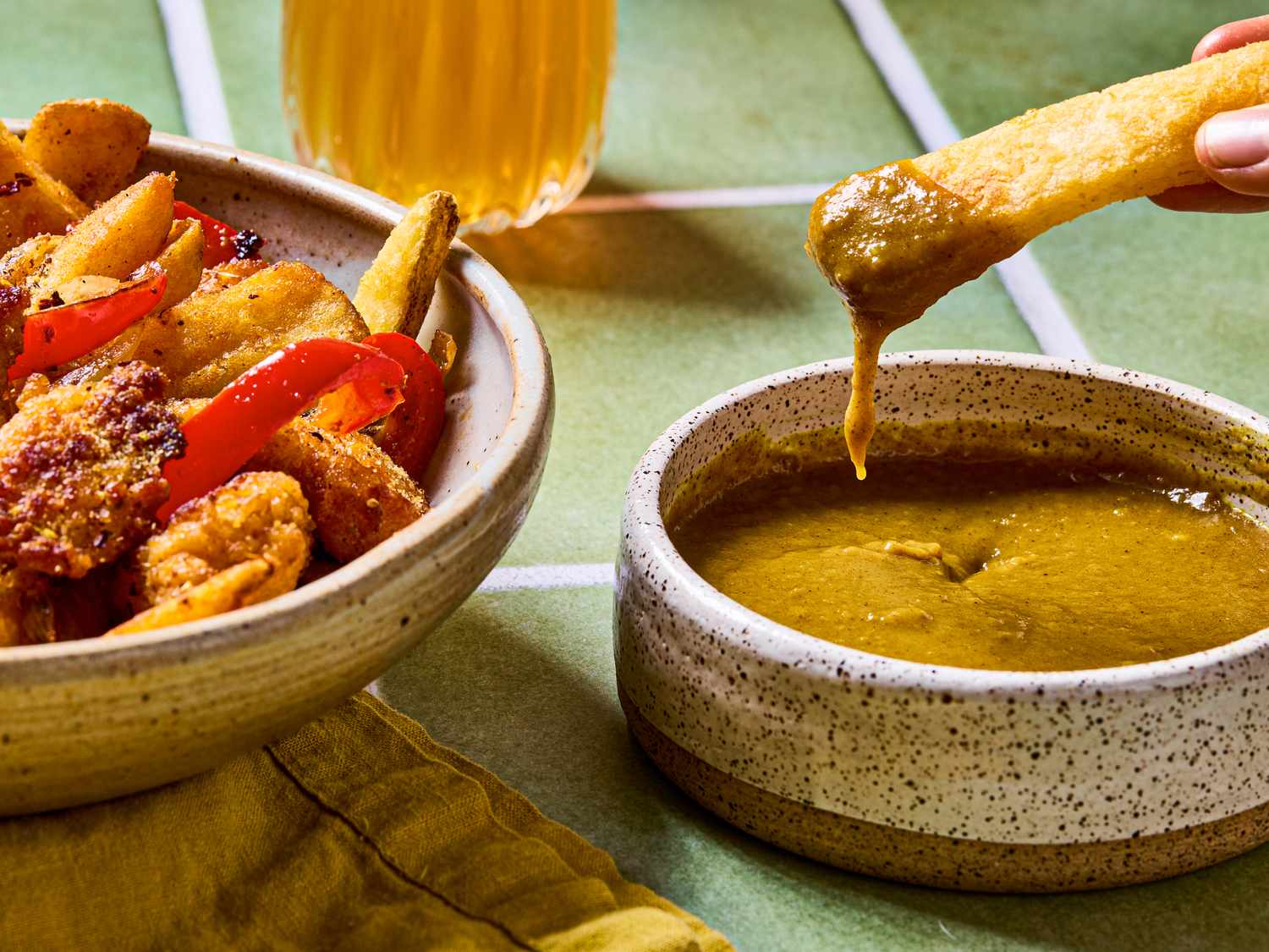 A bowl of battered and fried food with a dipping sauce and what appears to be a beverage in the background