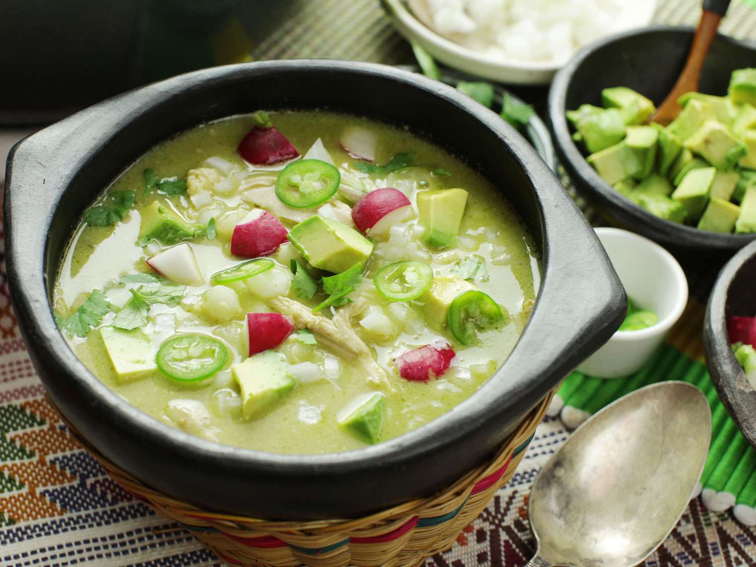 A bowl of green pozole topped with radishes, avocado, and jalapeño slices.