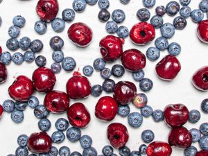Blueberries and pitted cherries scattered on a white surface
