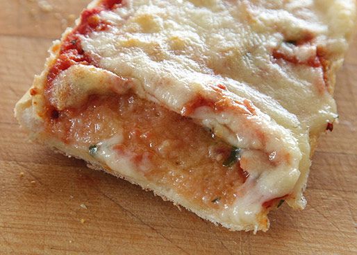 A piece of French bread with the cheese pushed back from the edge of the bread