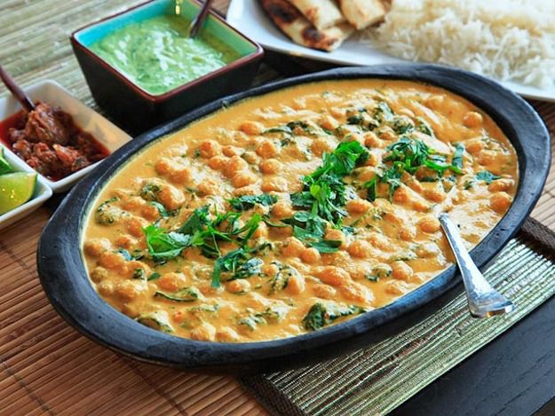 Earthenware bowl of chickpea curry with accompaniments in the background