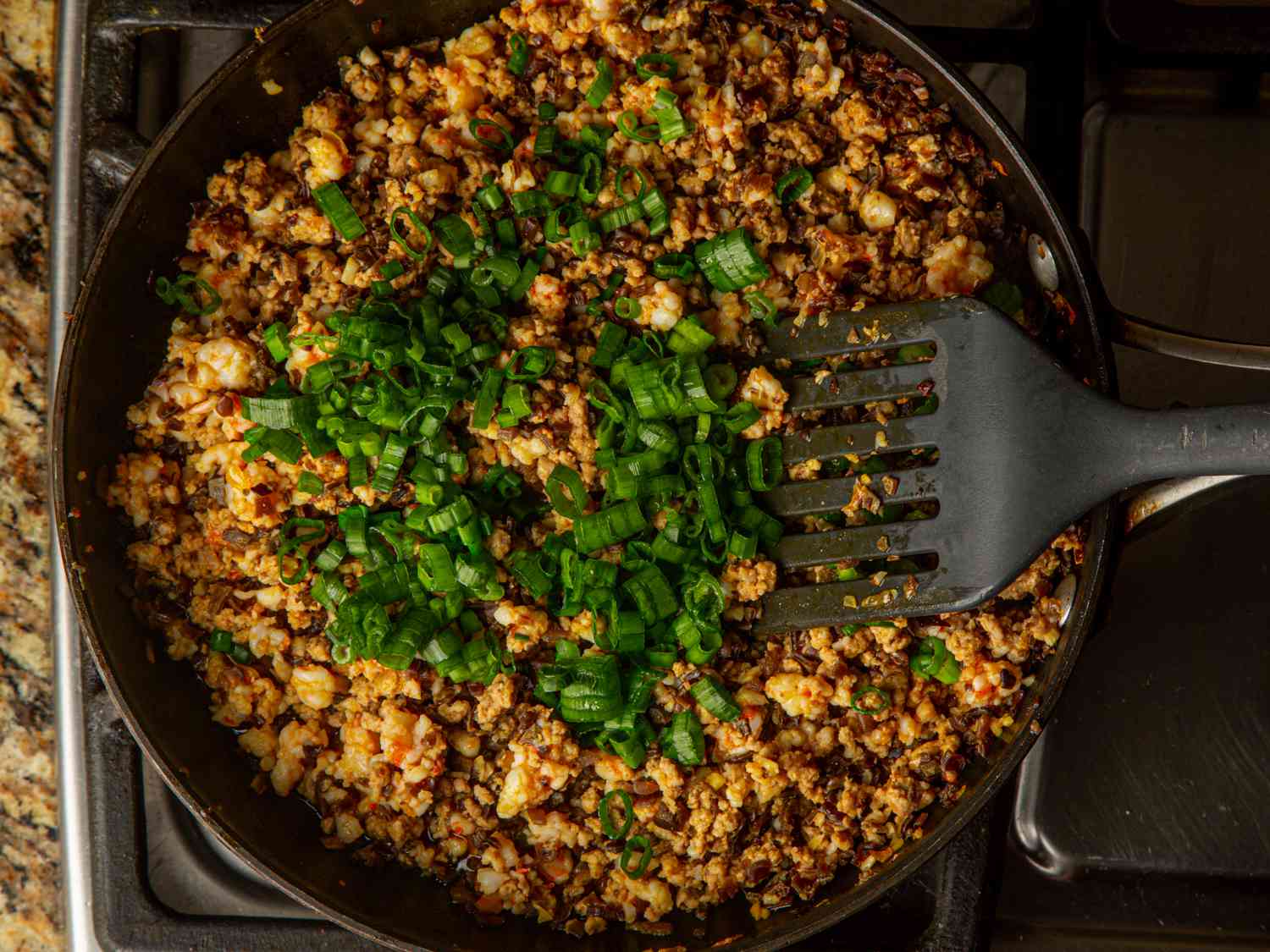 Adding green onions to skillet with shrimp, pork, and mushrooms