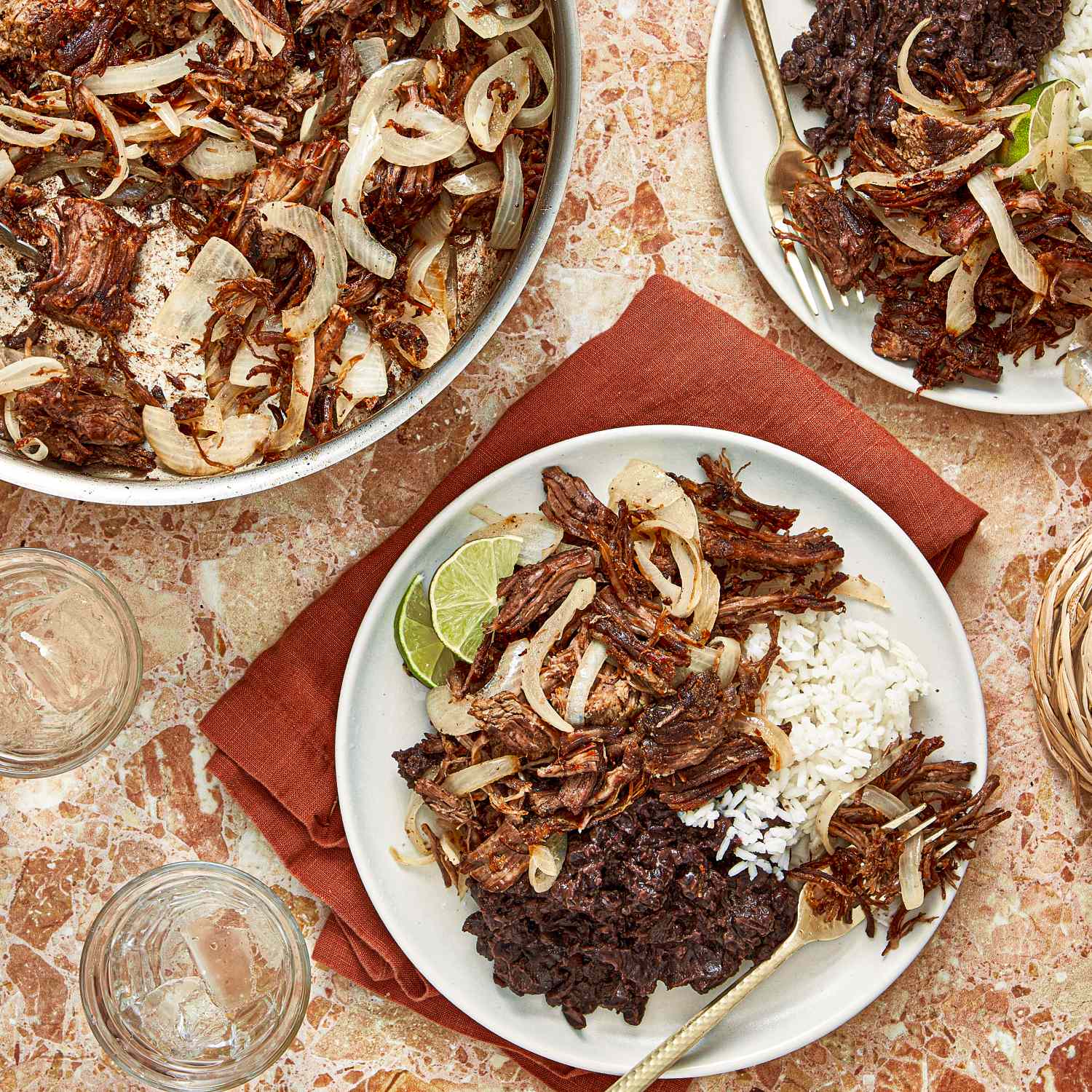 Three plates of Vaca Frita with rice black beans and lime slices on a table setting