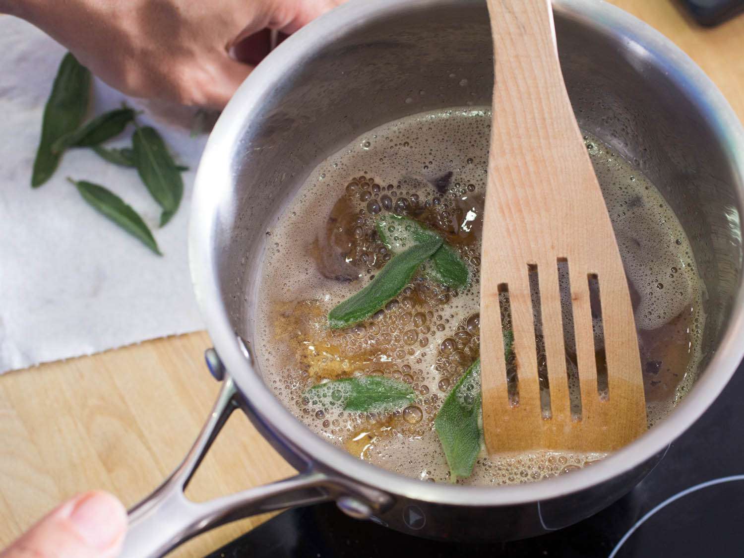Frying sage leaves in brown butter, stirring with a wooden slotted spoon.
