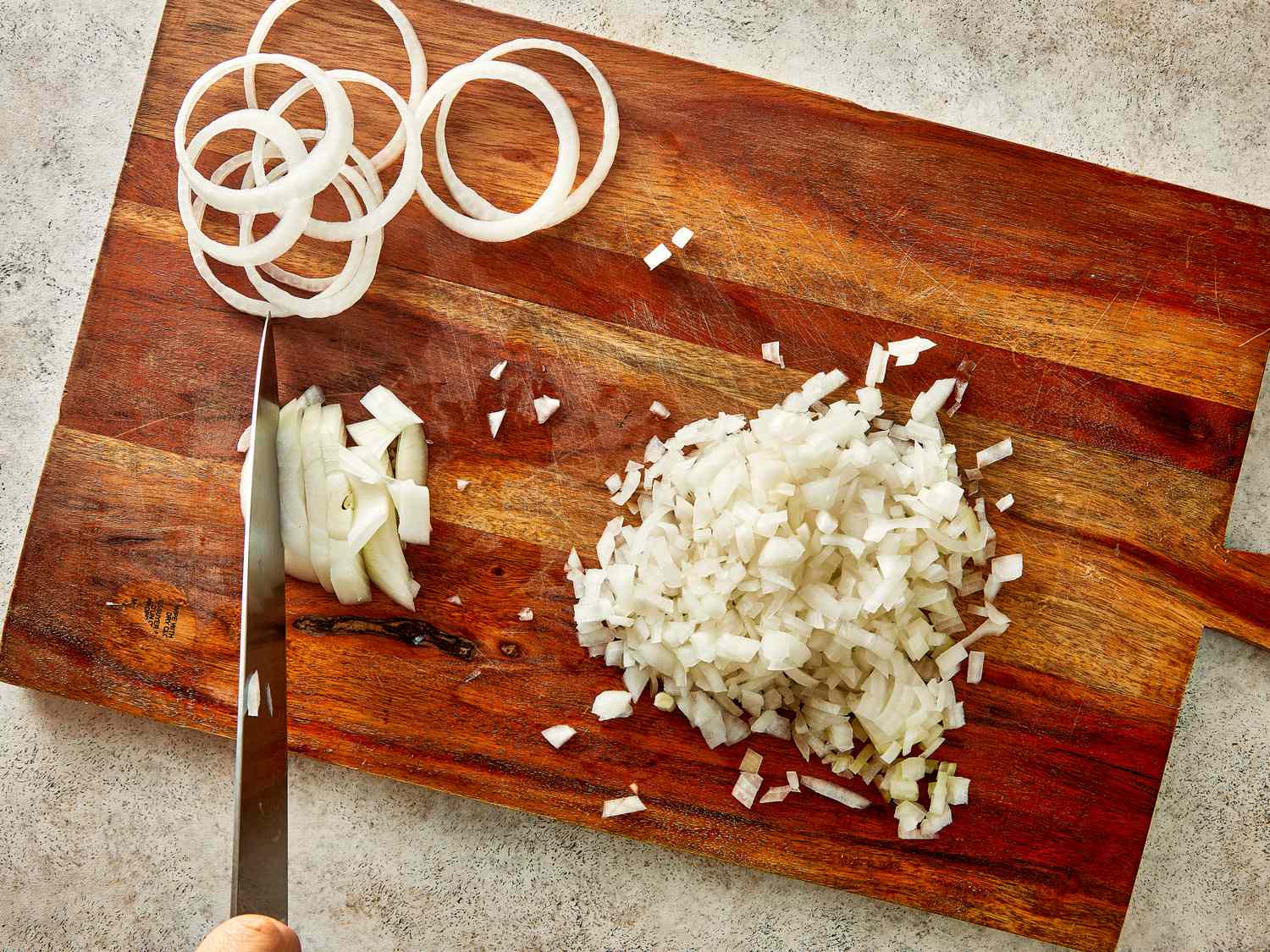 Chopped and sliced onions on a wooden cutting board knife in hand cutting onions
