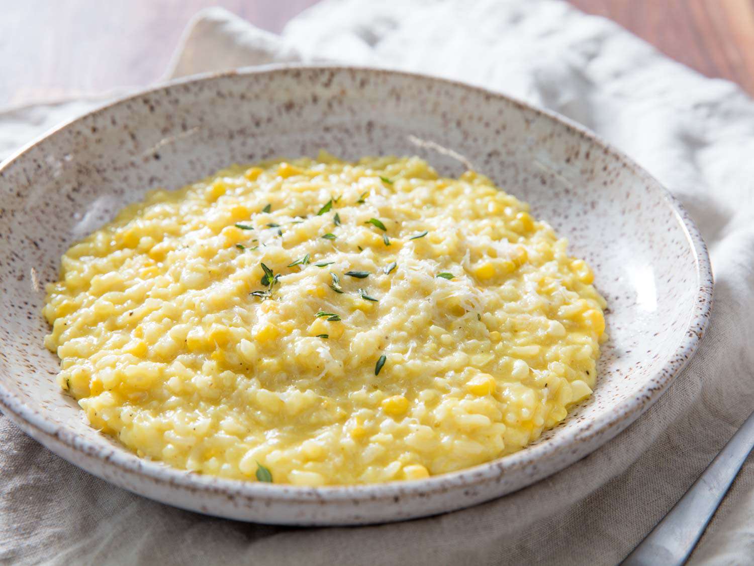 A shallow earthenware bowl of pressure cooker corn risotto, lightly sprinkled with thyme leaves.
