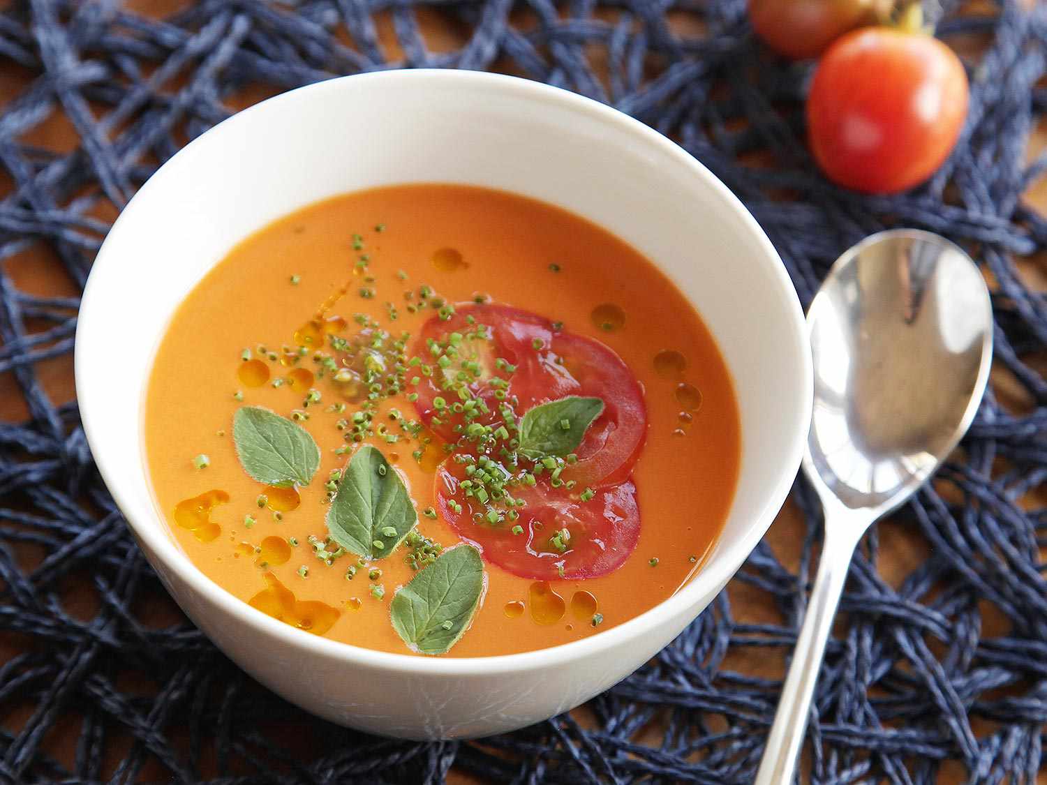 Bowl of gazpacho garnished with olive oil, fresh herbs, and tomato