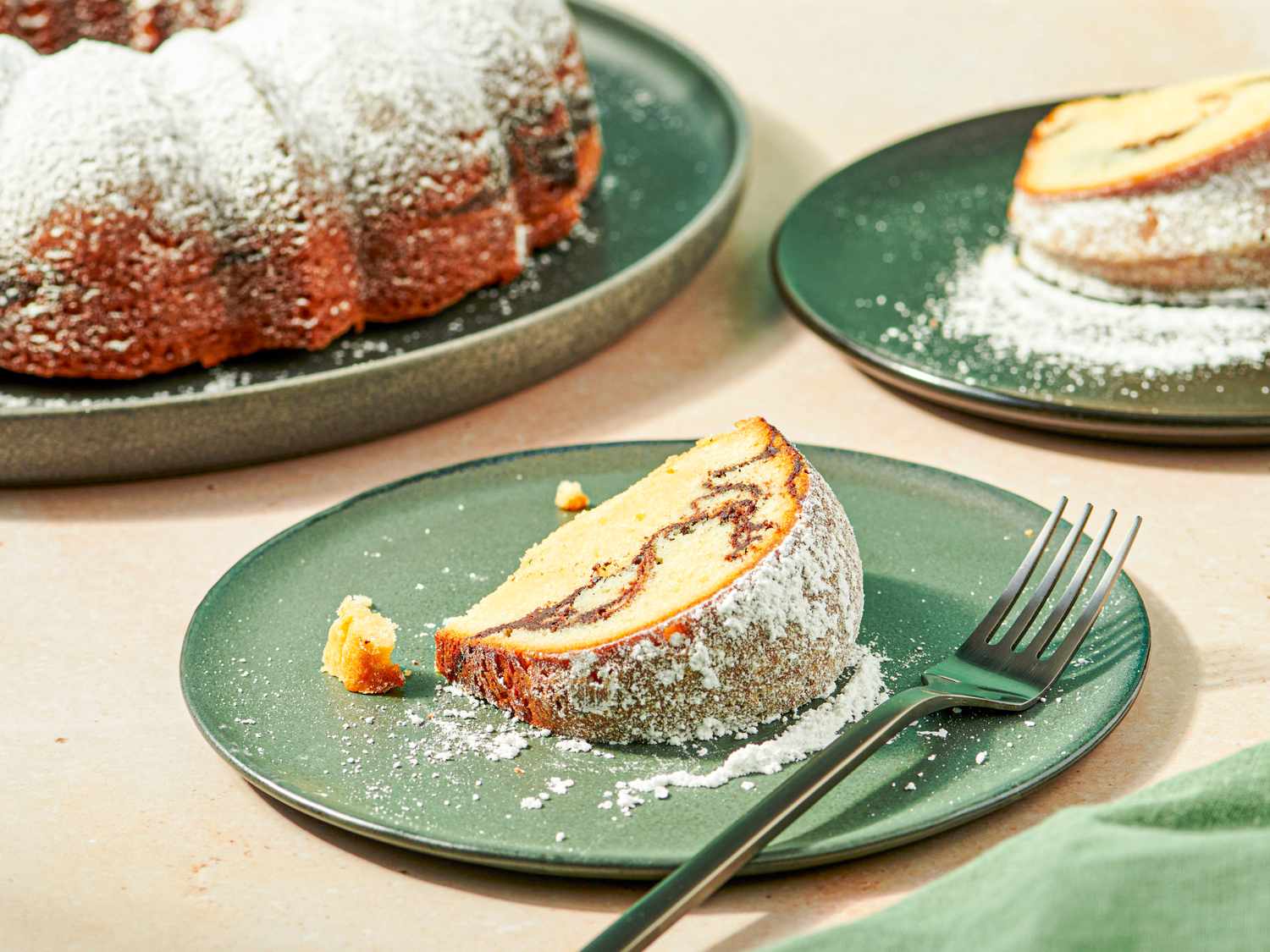 Slices of bundt cake dusted with powdered sugar on green plates one slice served with a fork