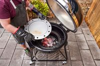 A person places a grill plate in the Weber 18201001 Summit Kamado E6 Charcoal Grill