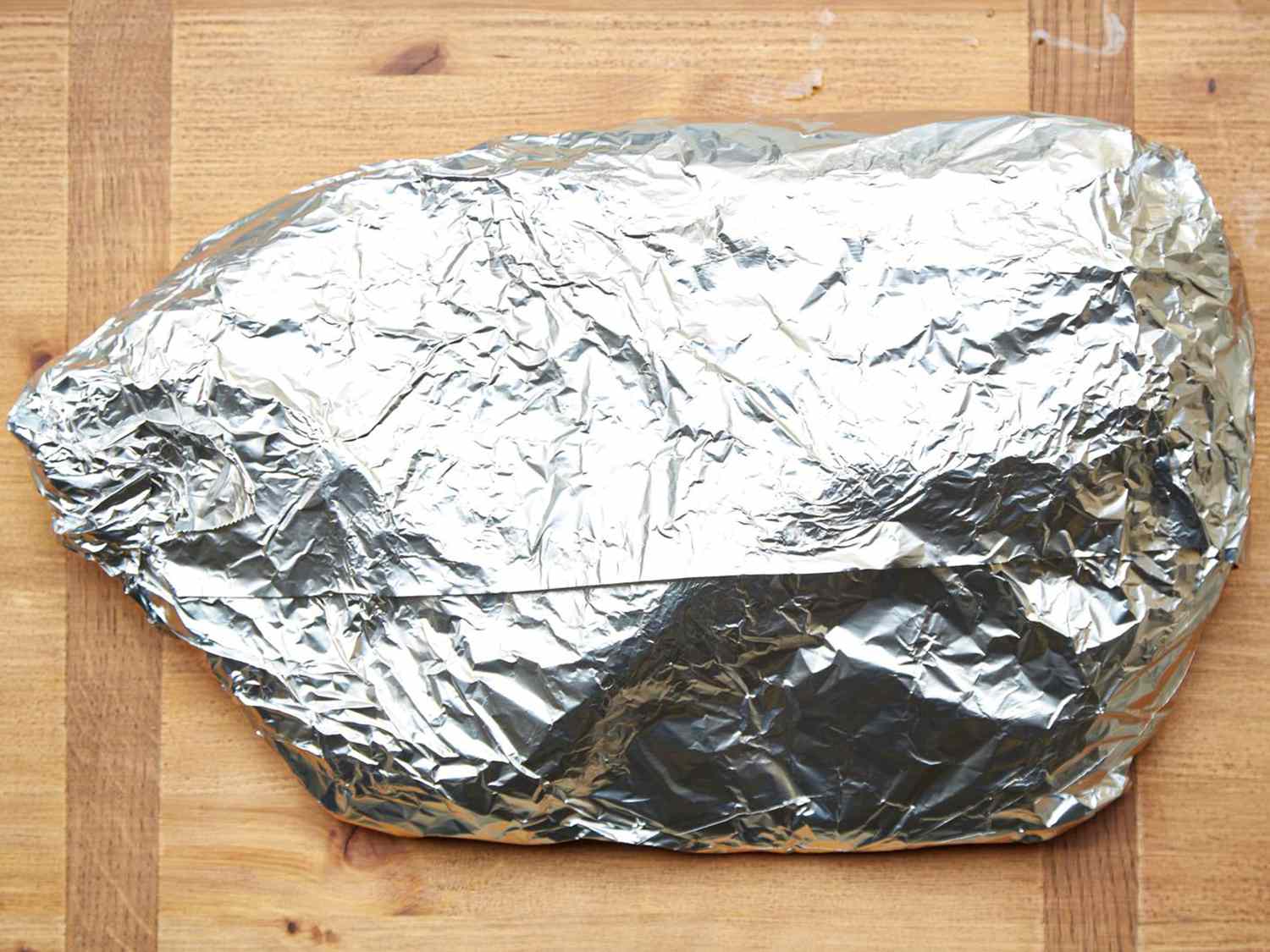 Brisket wrapped in aluminum foil placed on a wooden surface