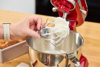 A person holds up the whisk attachment for the KitchenAid Artisan Mini 3.5-Quart Tilt-Head Stand Mixer