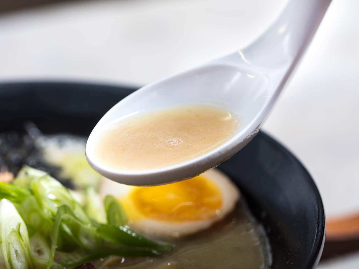 A spoon lifting miso tori paitan broth out of a bowl of noodles.