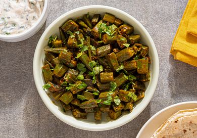 A bowl of spiced okra garnished with cilantro served on a table with side dishes