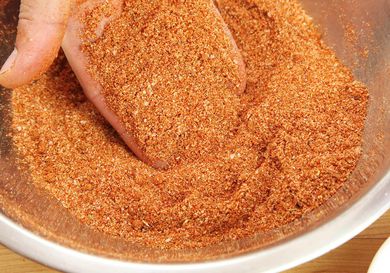 A hand lifting some dry bbq rub out of a metal mixing bowl.