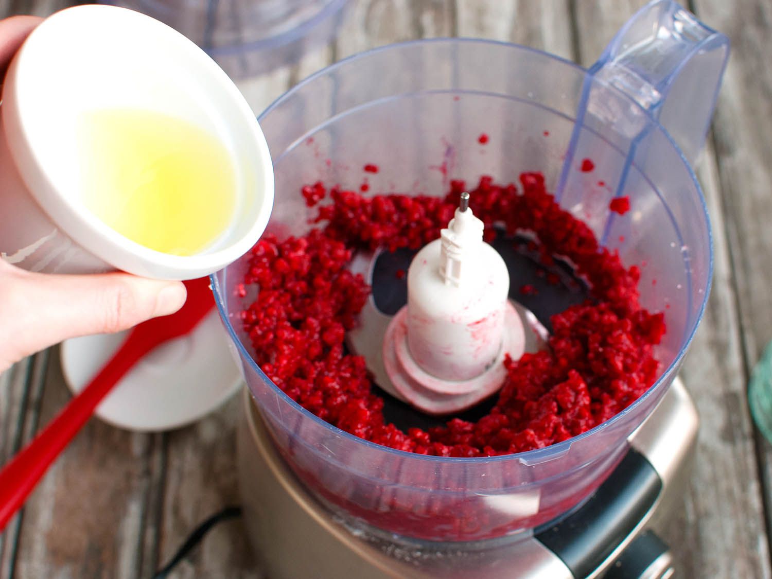 Egg white being poured into a food processor filled with pureed frozen raspberries to whip up fruit mousse