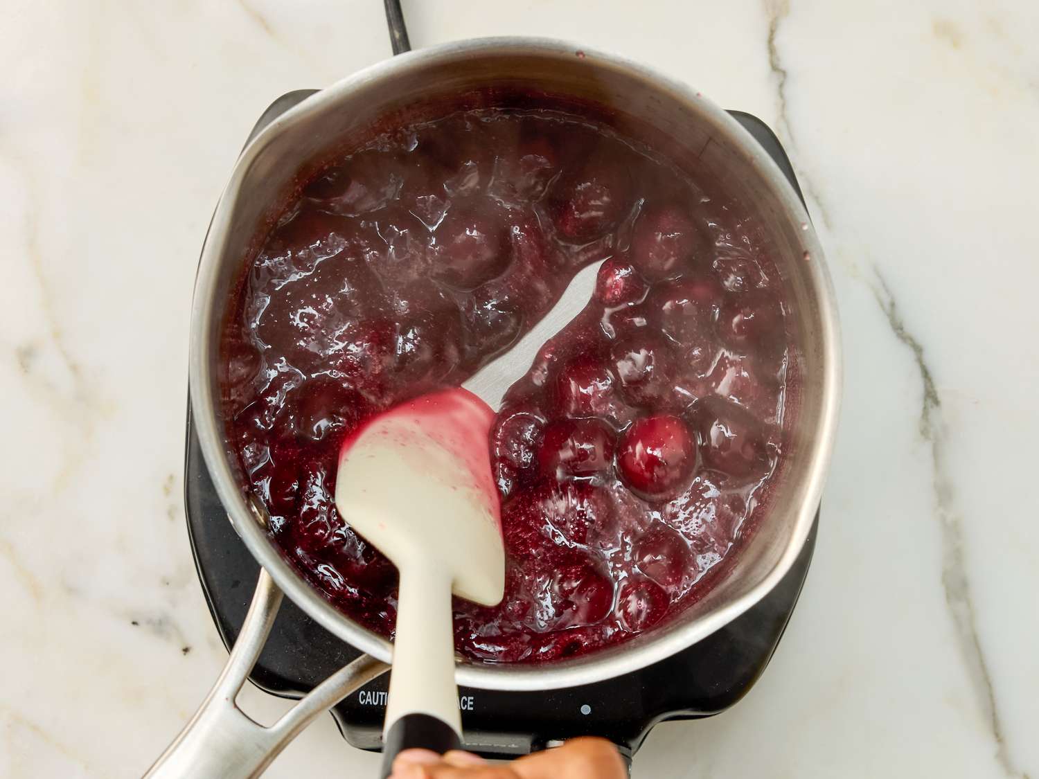 Cooking cherries in a saucepan with a spatula being used to stir them