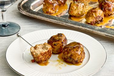 Turkey meatballs glazed with maple mustard served on a white plate with a serving tray in the background