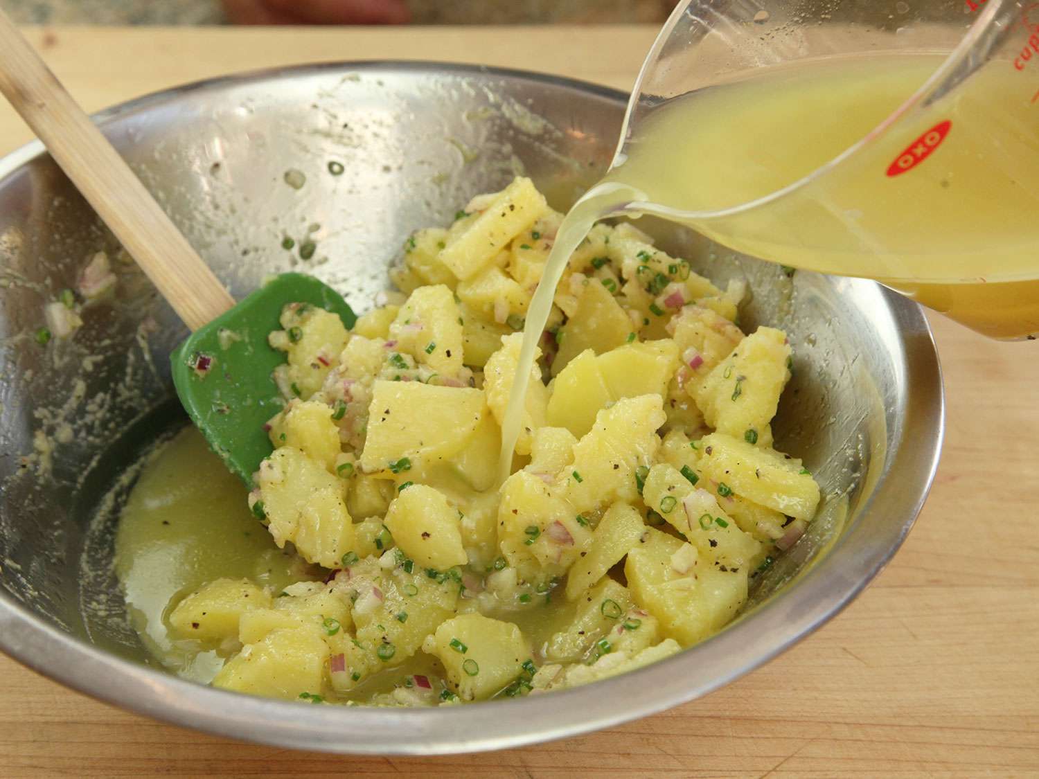 Folding together ingredients for Austrian potato salad: potatoes, onion, chives, and chicken broth.