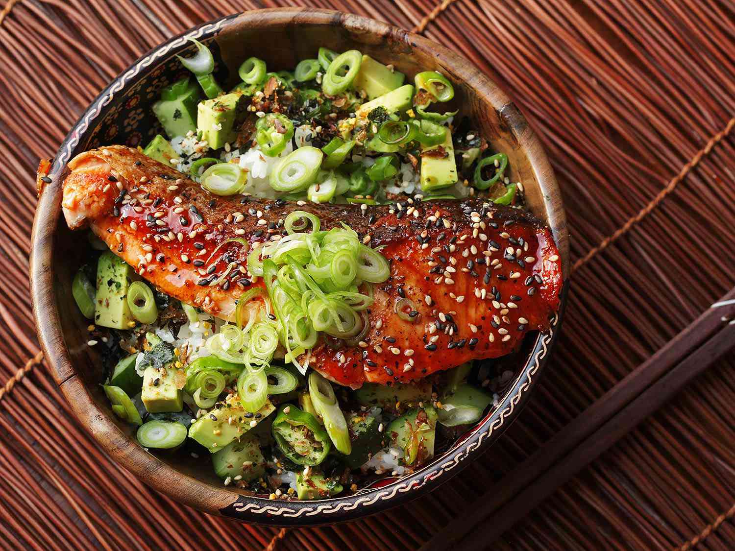 Overhead of teriyaki-glazed salmon rice bowl with sliced scallions and furikake. 