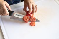A person thinly slicing a tomato