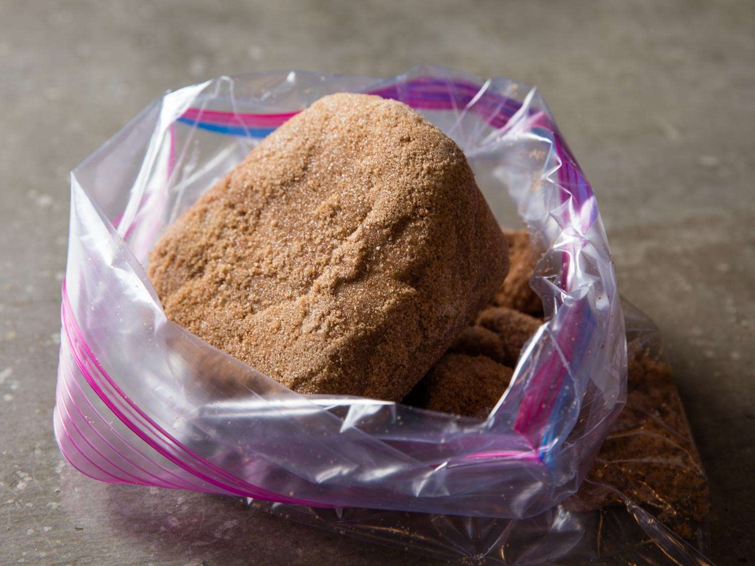 A large, hardened lump of brown sugar in a zip-top bag, the opening of which has been rolled back and propped open.