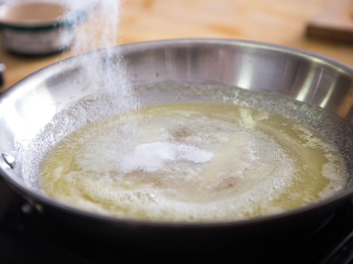 Adding sugar to bubbling melted butter in a saute pan.