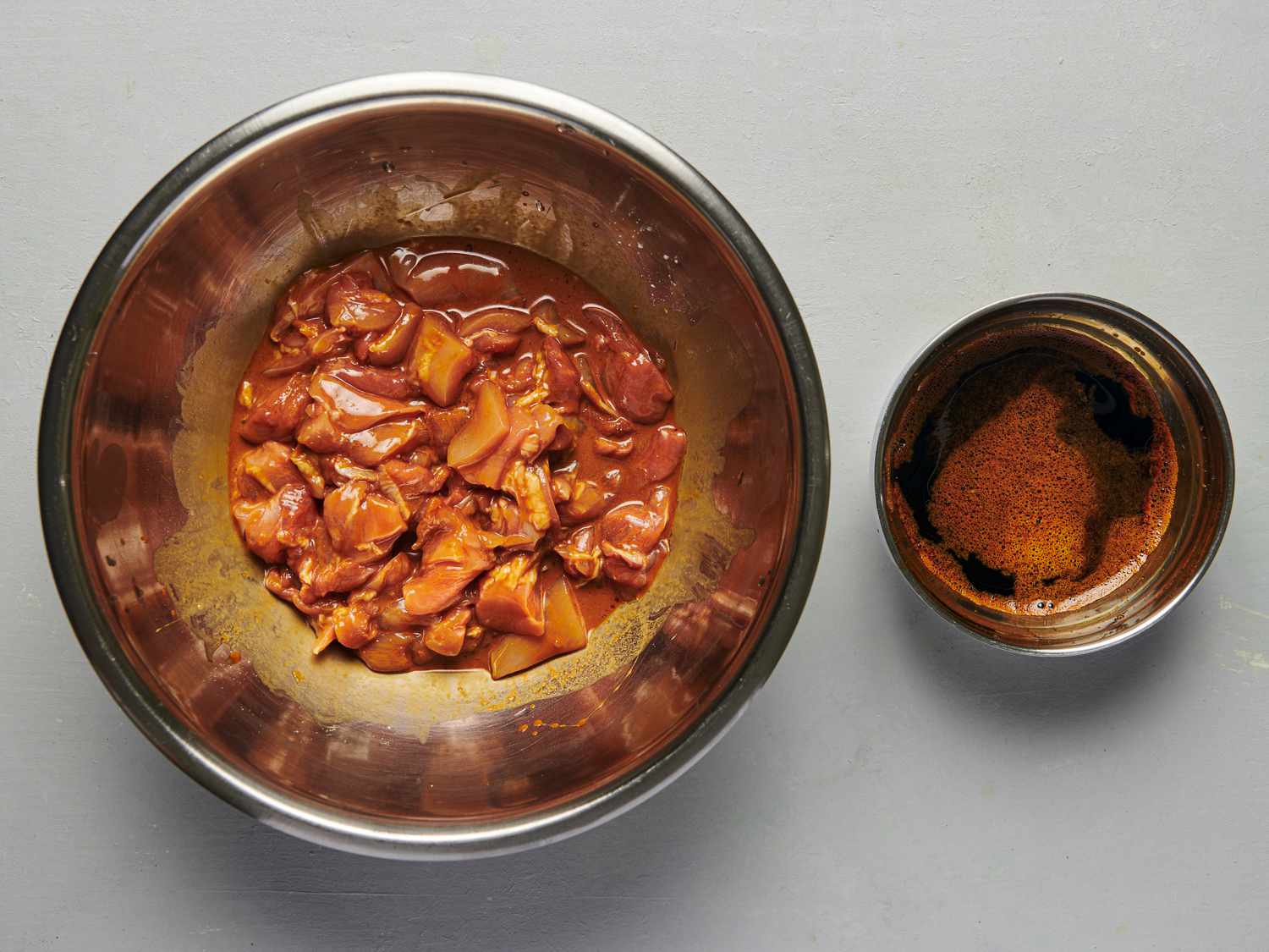 Chicken coated thoroughly in marinade inside a large bowl (after whisking in cornstarch and baking soda), next to a smaller bowl containing the reserved marinade.