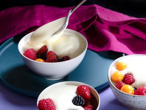 Zabaglione being spooned into a bowl of fruit with two other topped bowls in the foreground.