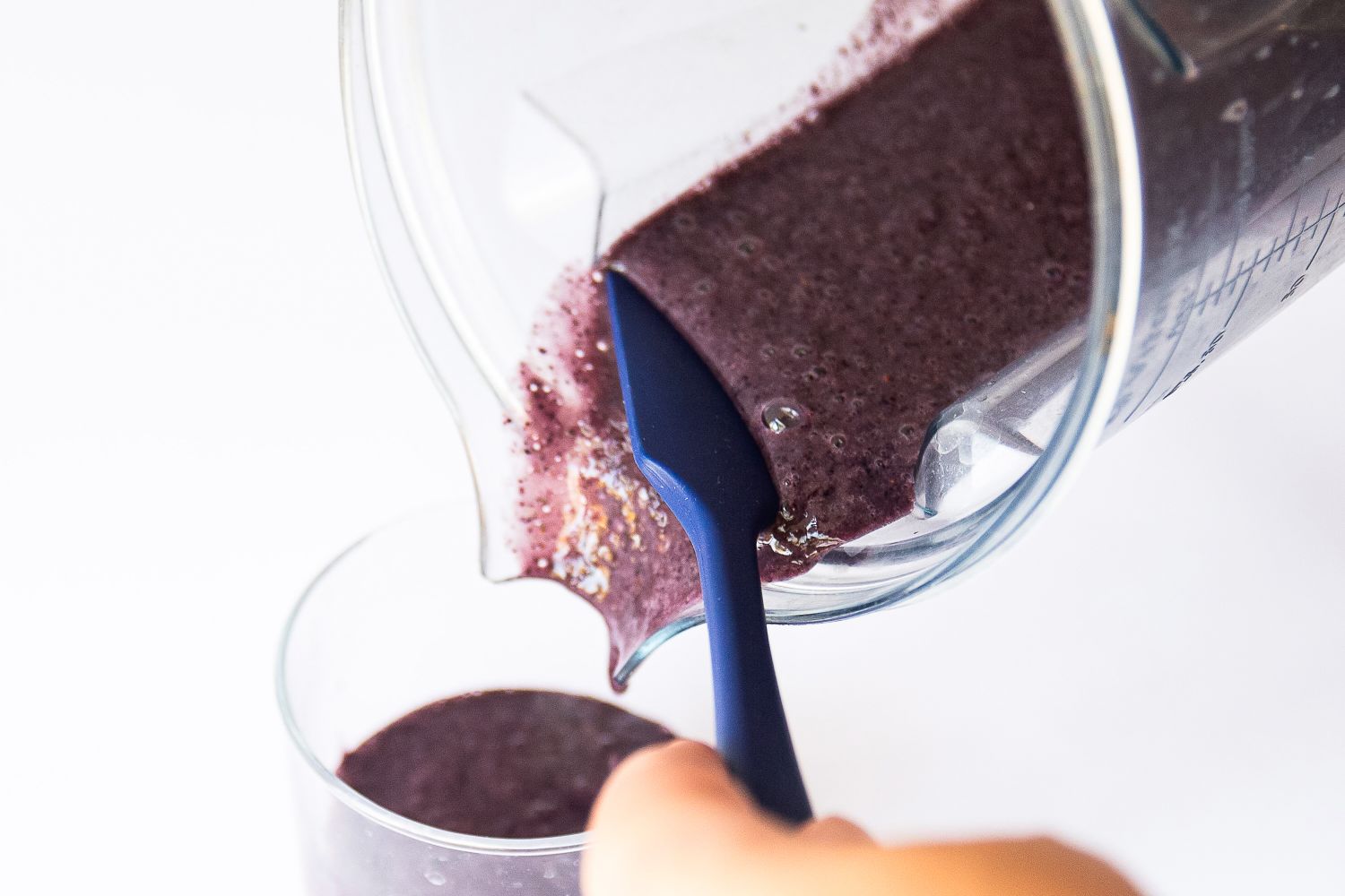 A person using a blue silicone spatula to pour a smoothie from a blender