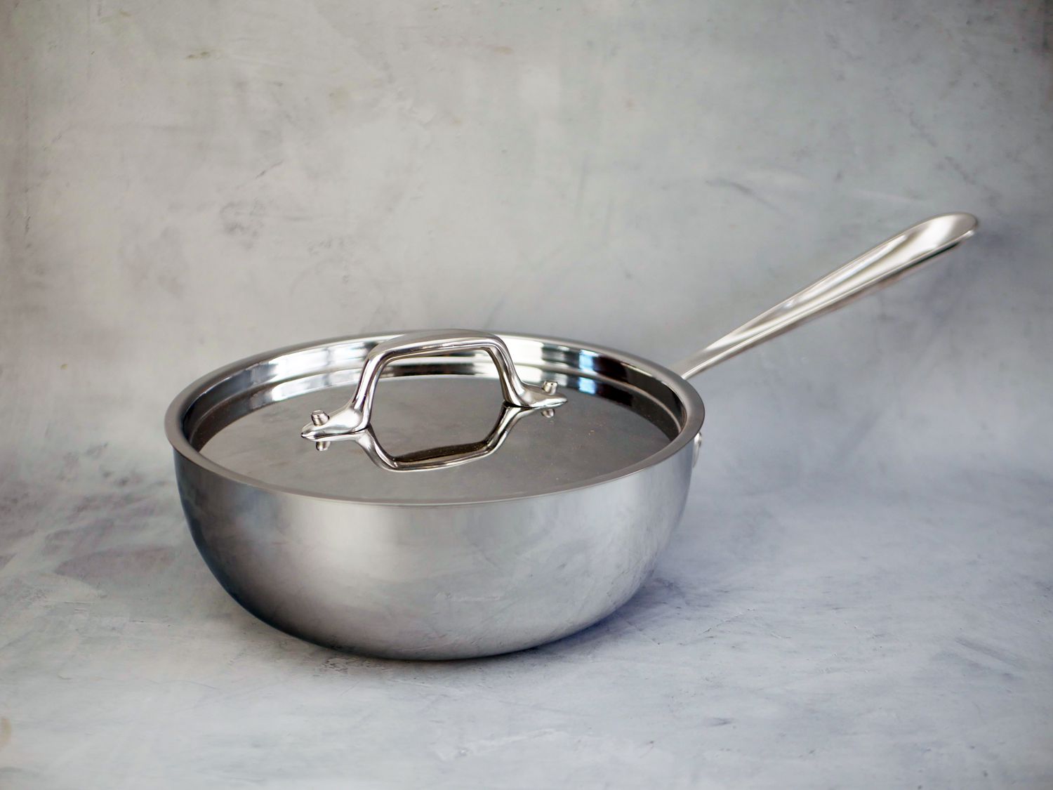 all-clad saucier with lid on a gray textured background