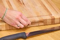 A hand adjusting a John Boos Reversible Maple Wood Cutting Board with Juice Groove on a table near a serrated kitchen knife