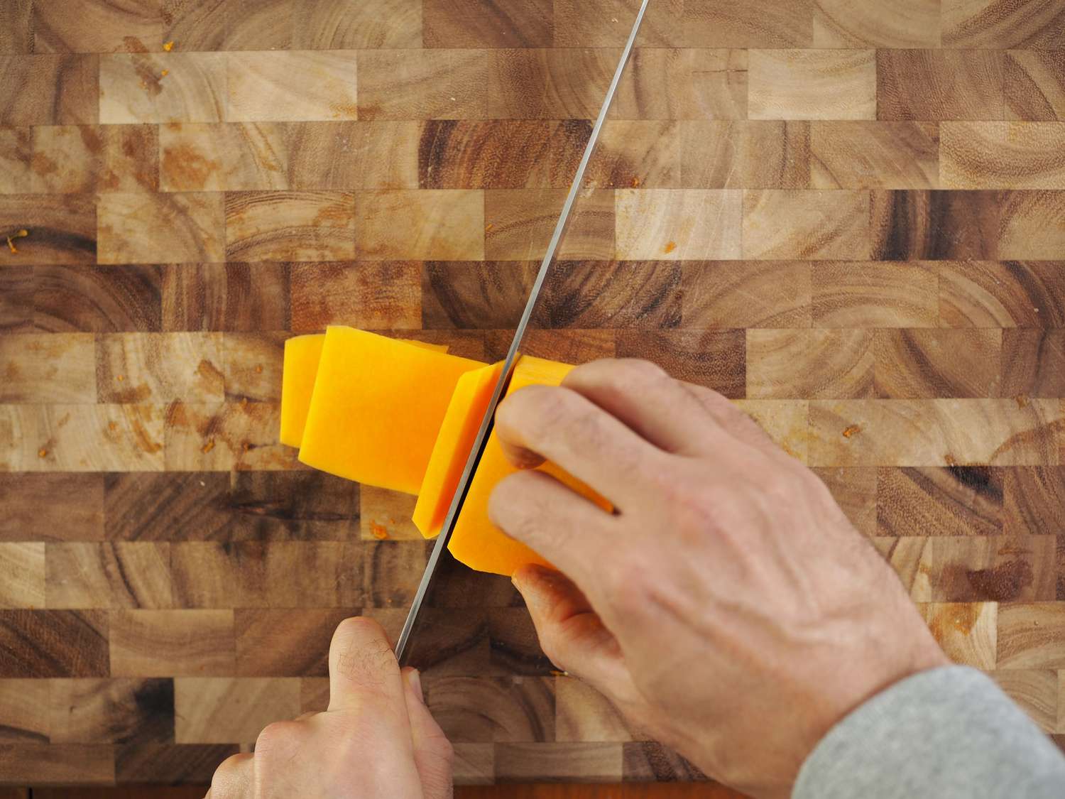 The neck of a butternut squash being cut into thin planks so that it can then be cut into small cubes.
