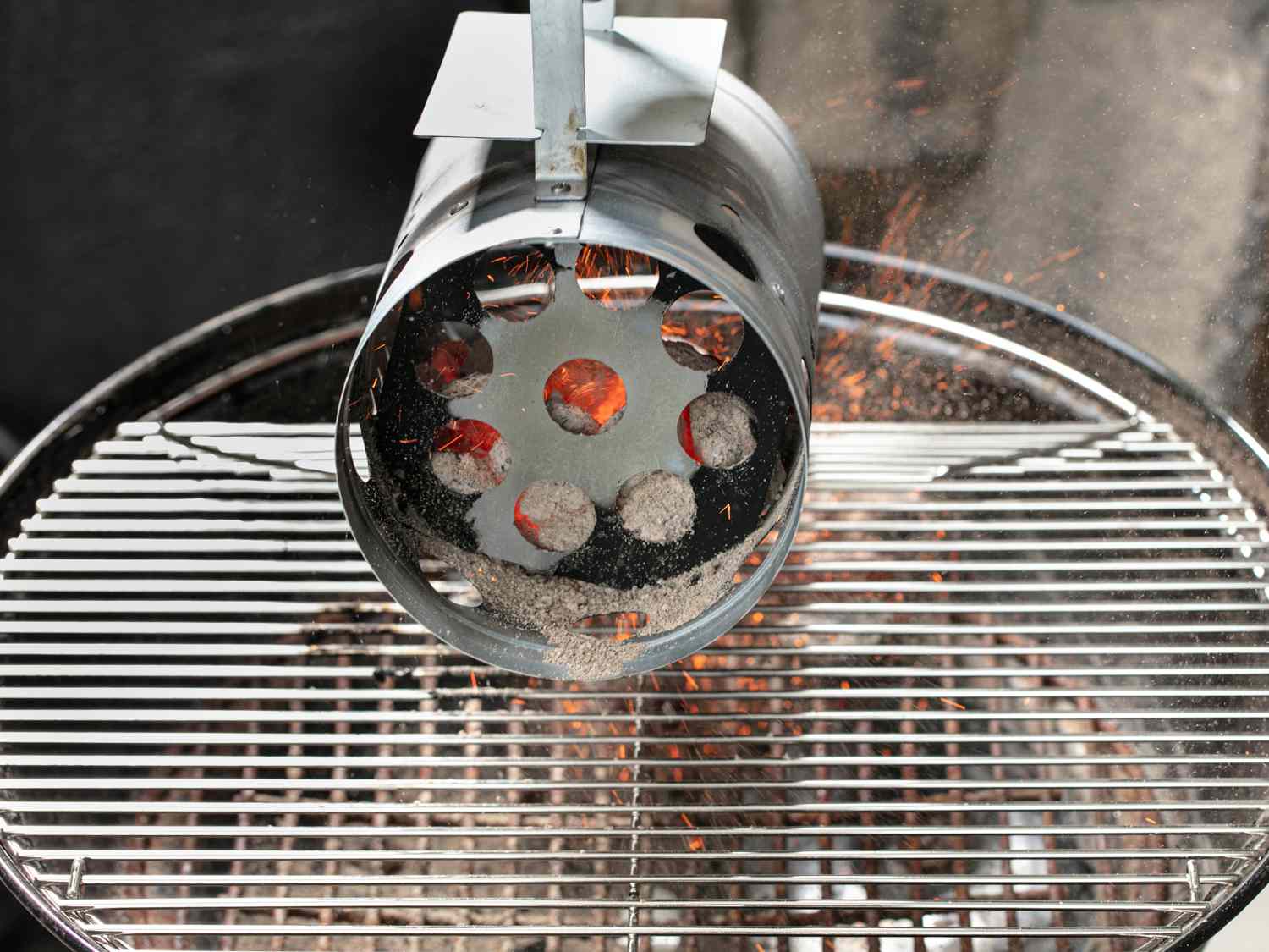 Charcoal being poured into grill from a starter for Peruvian grilled chicken.