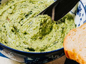 Butter being scooped from a bowl with a knife loaf of bread in the foreground