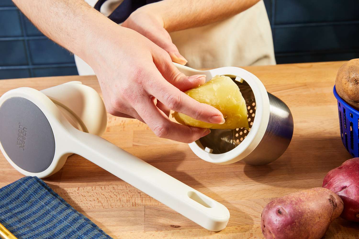 A person placing a cooked, peeled potato into a potato ricer's hopper.
